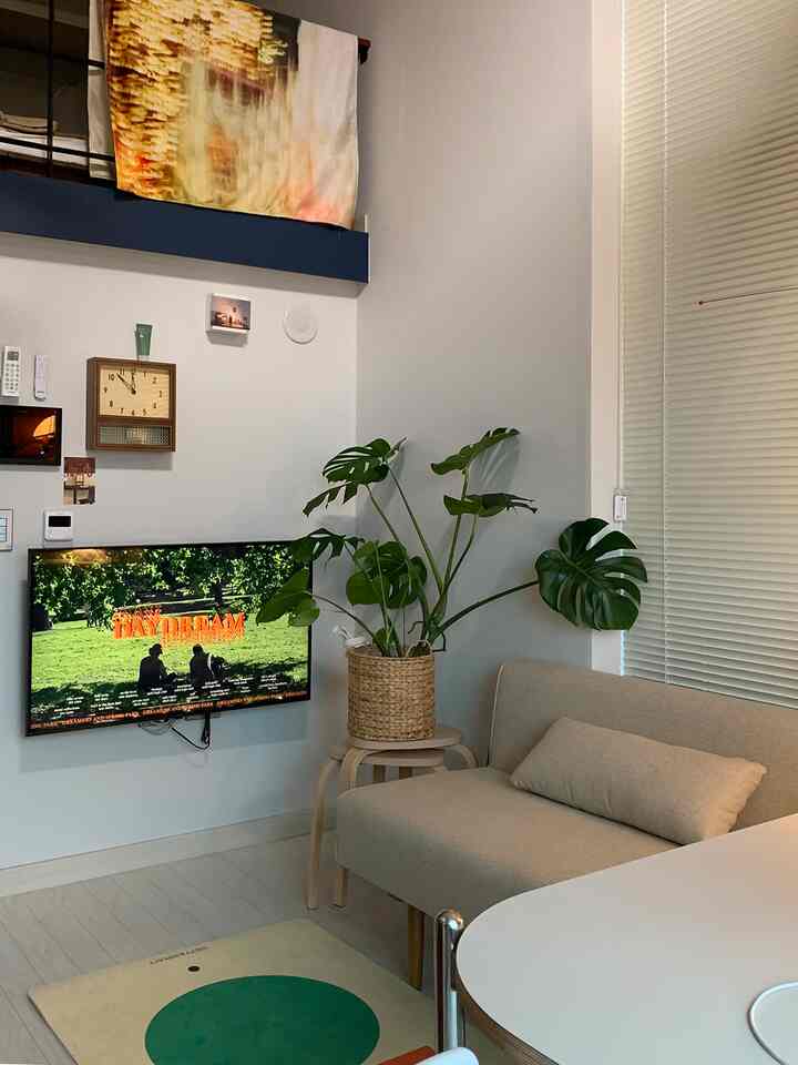 ベージュとナチュラルトーンの小さなリビング、ベージュのソファと壁掛けテレビ、観葉植物が配置された雰囲気のある空間。