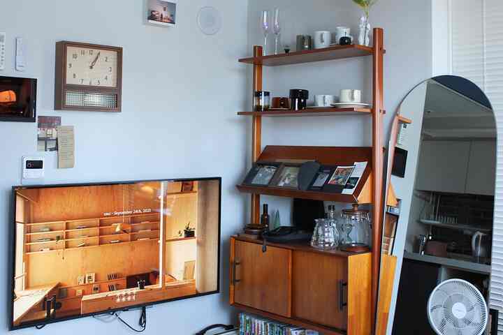 ホワイトとウッドトーンのリビング、レトロなキャビネットと壁掛けテレビ、楕円形の鏡が配置された落ち着いたインテリア