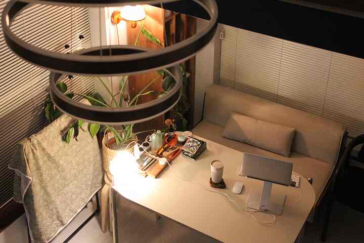 ベージュ調のワンルーム、ソファとテーブルにはノートパソコンとファブリックが配置された居心地の良い在宅勤務スペース