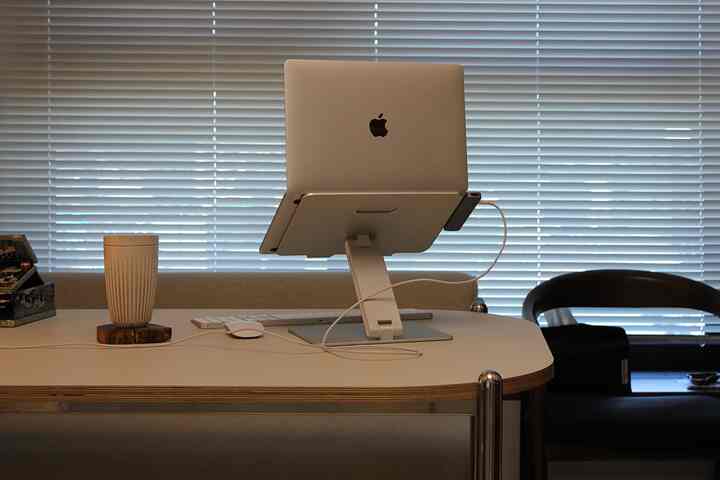 白を基調としたホームオフィス、デスク上にノートパソコンとモニタースタンドが配置された整然とした作業空間