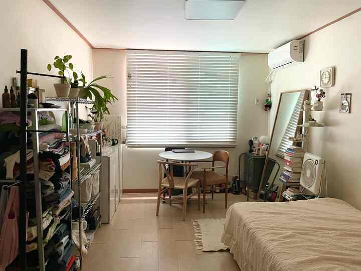 白とナチュラルカラーの調和が取れたコンパクトな寝室、小さなダイニングテーブルと棚、整頓された収納スペースがある空間