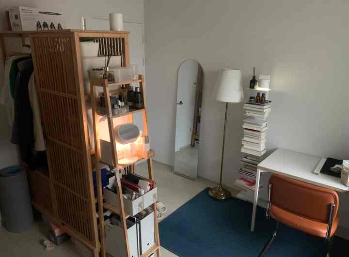 白い壁とナチュラルウッド調の家具が置かれたコンパクトな部屋、デスクや椅子、フロアランプが配された雰囲気のあるホームオフィス