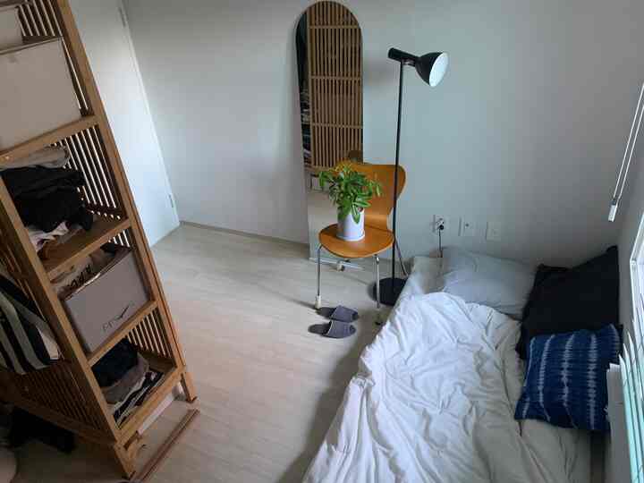 ホワイトとウッドトーンが基調のコンパクトな寝室、整ったワードローブとデスクが配置されたミニマルな空間