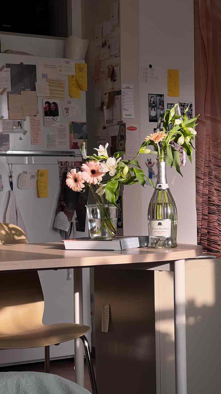 ベージュと白のトーンのキッチン、ダイニングテーブルに花瓶と本が置かれた温かみのある印象的な空間