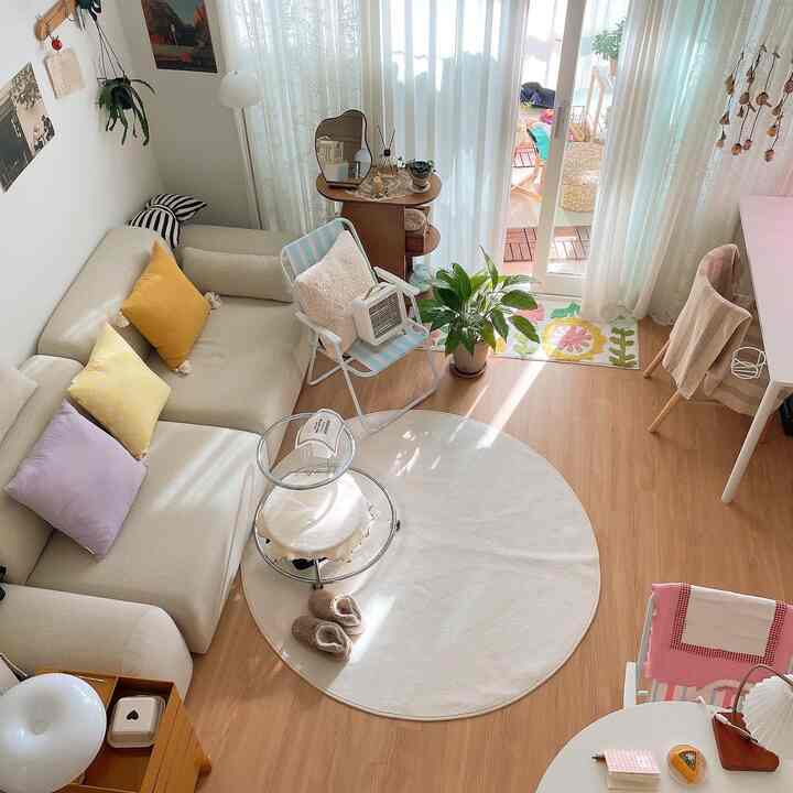 ナチュラルな木目調フローリングとベージュのソファ、白いカーテンとラウンドラグが配置された明るいリビング