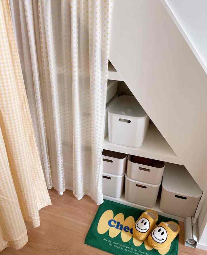 明るいナチュラルカラーの階段下三角形収納スペース、カーテンと白い収納ボックスが配置された清潔感のあるインテリア