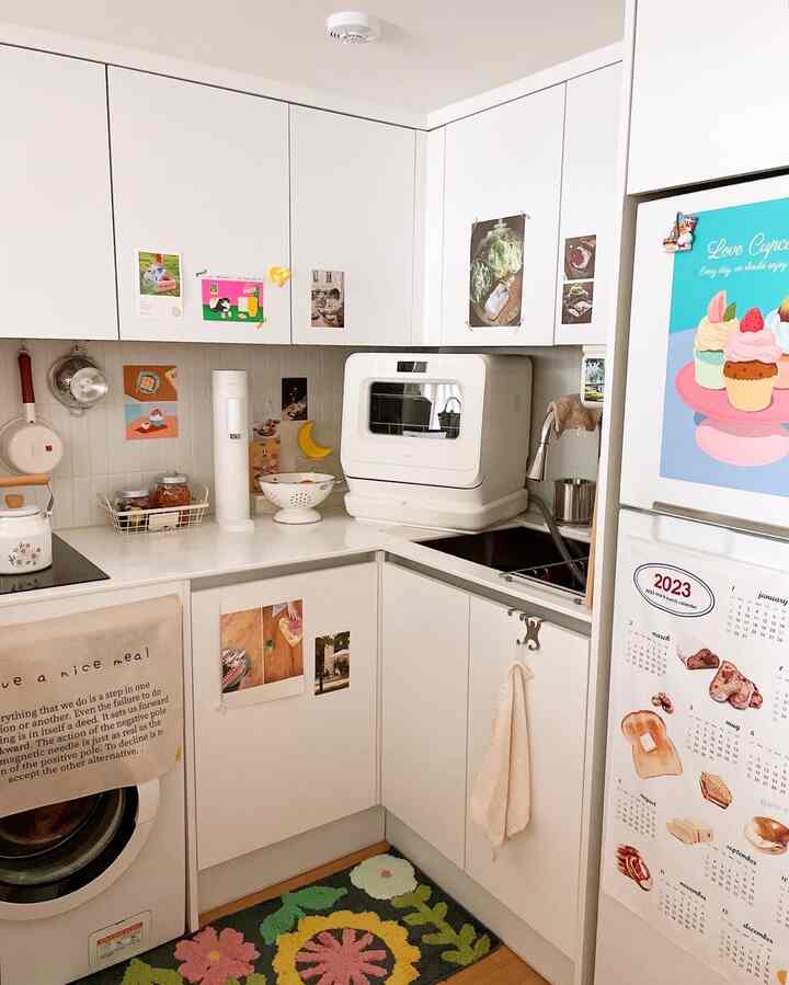 白を基調としたU字型キッチン、カラフルなバスマットと複数のポスターが配置された雰囲気のある空間