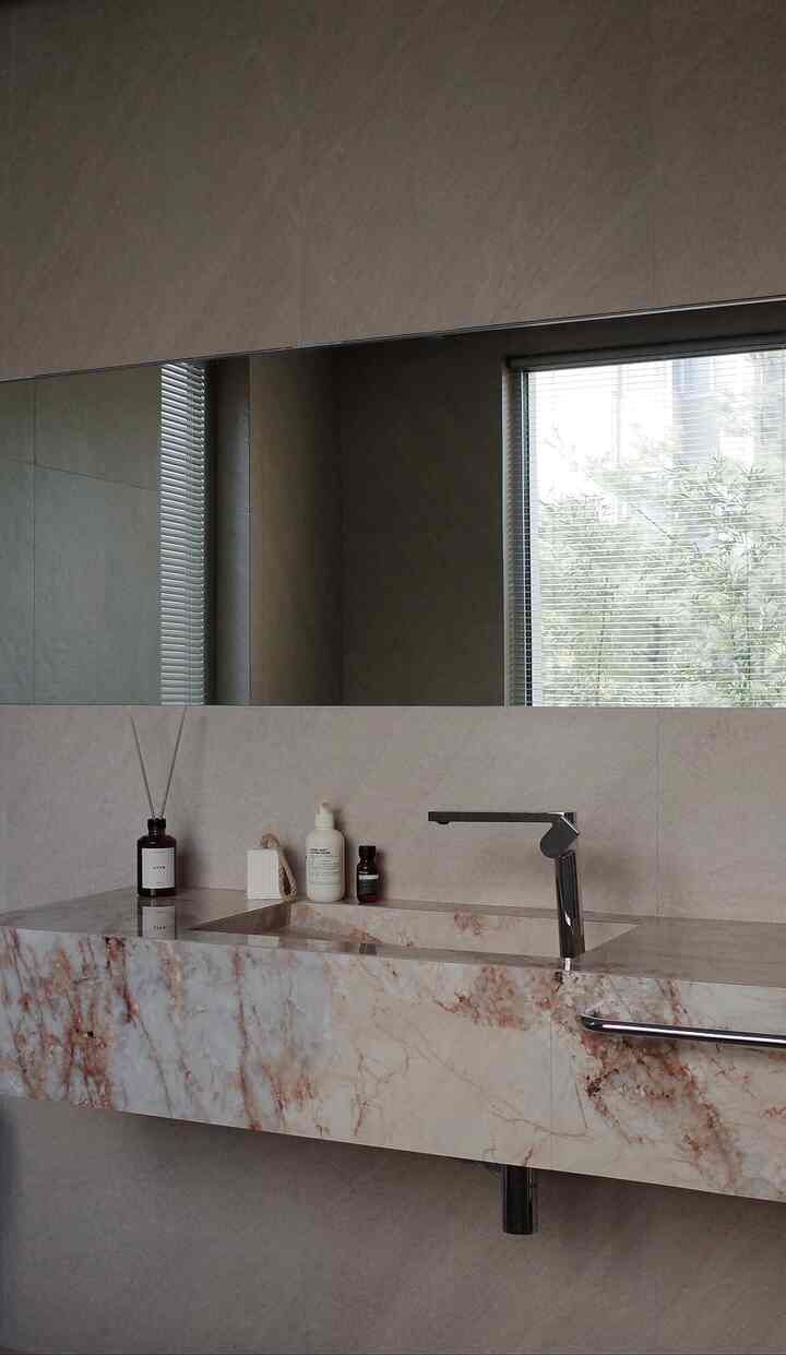 ベージュのナチュラルトーンのバスルーム、大理石の洗面台とクロームの蛇口、ディフューザーとハンドソープが配置された清潔感のあるインテリア