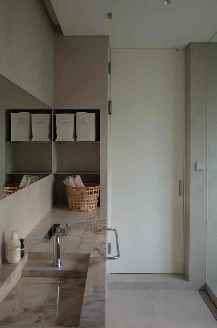 白とベージュの色調のバスルーム、大理石の洗面台と収納棚にタオルや小物が整頓された清潔感のあるインテリア