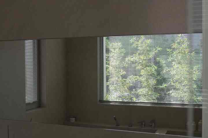 ナチュラルカラーの壁と窓の外に竹が見える大きな鏡が設置されたバスルームのインテリア