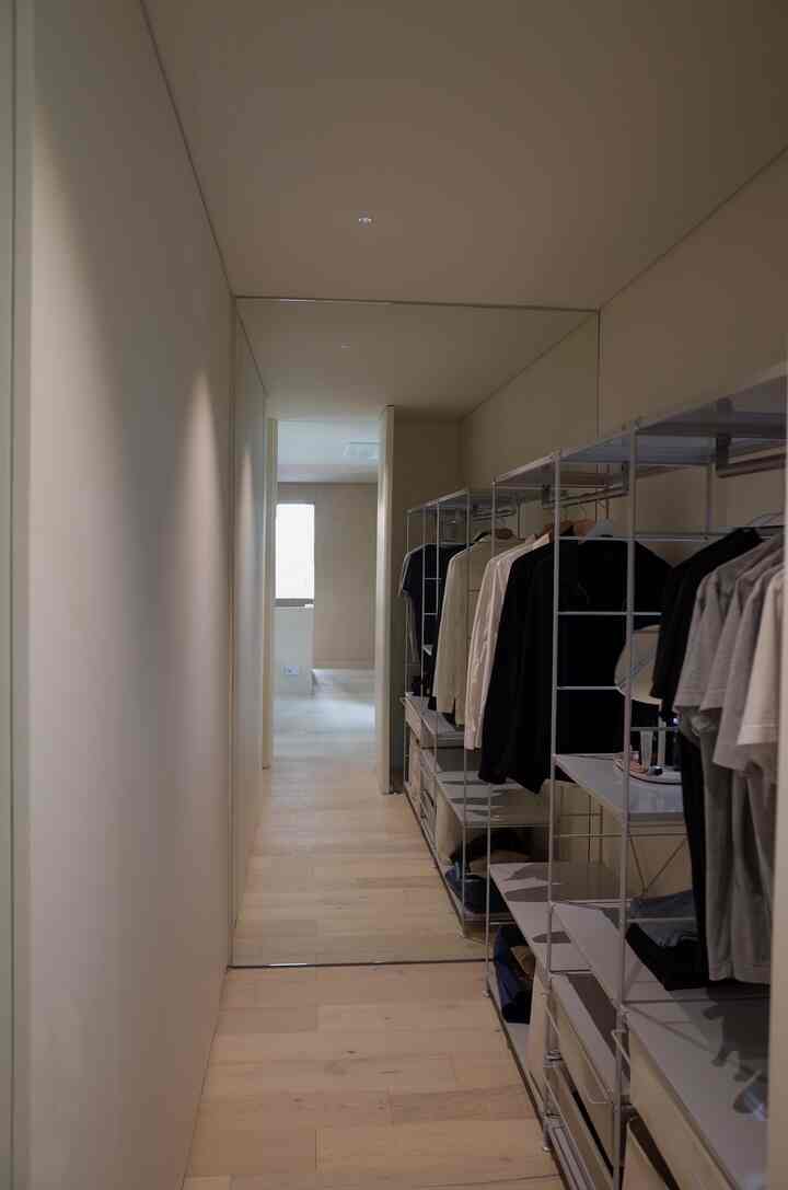 白い壁とライトブラウンの木製床を備えた狭く細長いクローゼット空間、清潔でナチュラルな雰囲気のインテリア