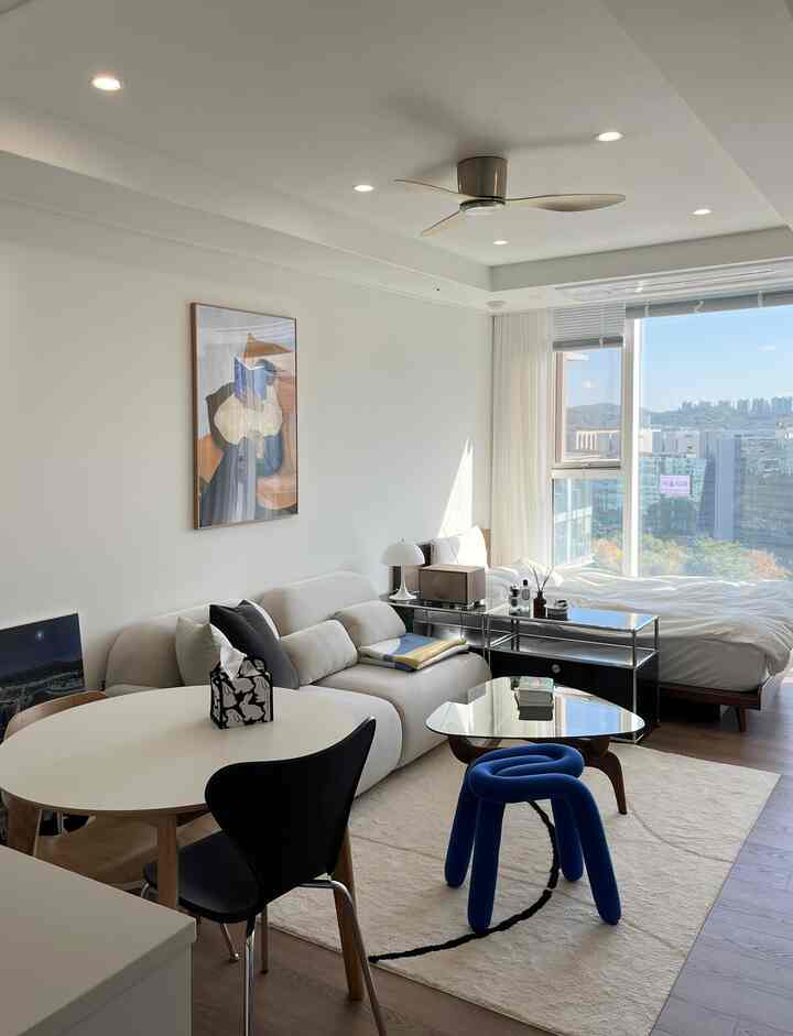 ホワイトとウッドトーンが調和するワンルームのリビング兼寝室、シーリングファンと清潔感のあるホテルライクなインテリア