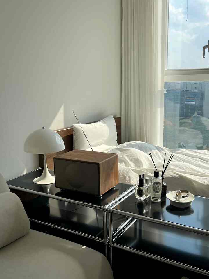 白と黒のトーンの寝室、木製ベッドフレームと黒の収納キャビネットが配置された自然光あふれるモダンなインテリア