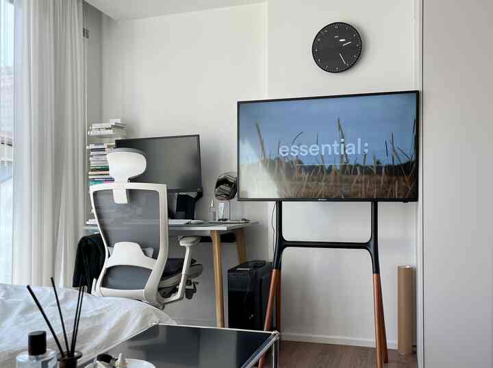 白を基調としウッドアクセントが融合したホームオフィス、コンピュータデスクとテレビスタンドが配置された清潔感のある作業空間