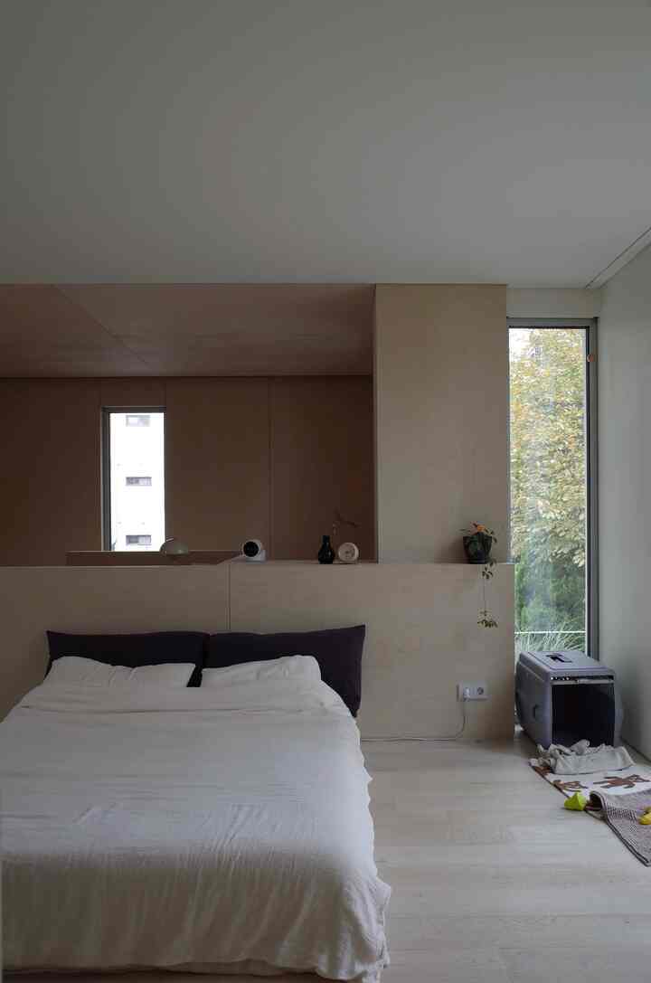 ベージュとアイボリーのトーンの寝室、中央に布団カバーを掛けたベッドと右側にペット用ケージが配置されたナチュラルなインテリア