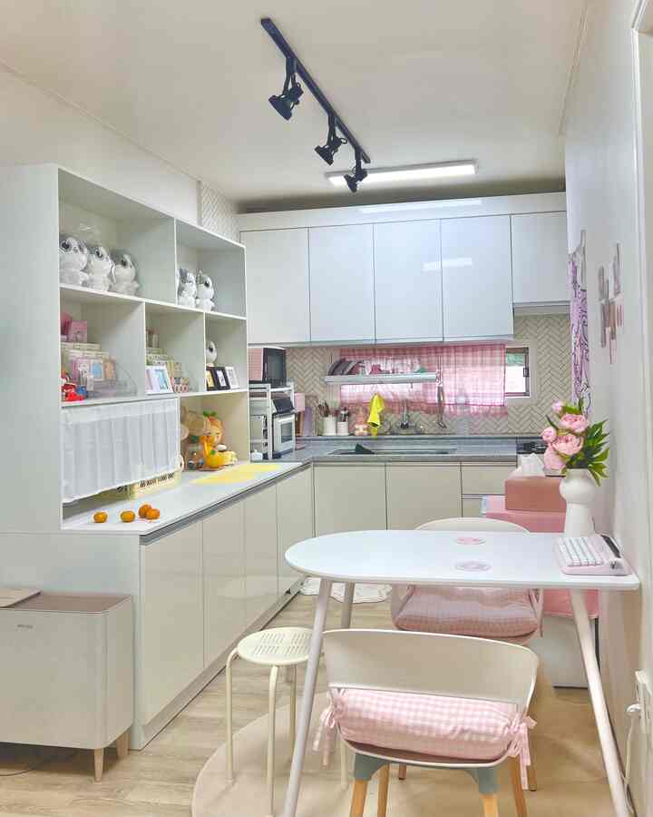 ホワイトとピンクのトーンが調和したコンパクトなキッチン、ダイニングテーブルとスツールが配置された雰囲気のあるインテリア