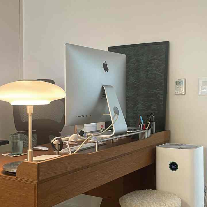 白と茶色のトーンのホームオフィス、ミッドセンチュリーモダンのデスクとiMacモニター、テーブルランプが配置された落ち着いたワークスペース