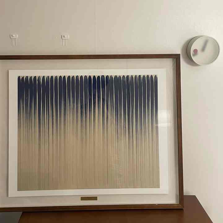 ネイビーのアートと木目調の額縁が配されたシンプルな壁面インテリア、白い壁に丸い時計を配置