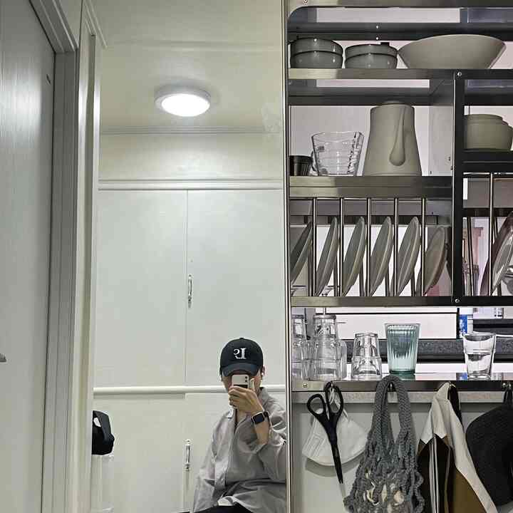 白い壁と大型全身鏡が配されたコンパクトなキッチン空間、シルバーのメタル棚と整然としたレイアウトが印象的なインテリア