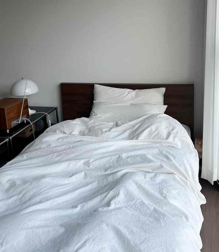 ホワイトの寝具とブラウンのヘッドボードが配置されたモダンな寝室、シンプルで清潔感のある雰囲気