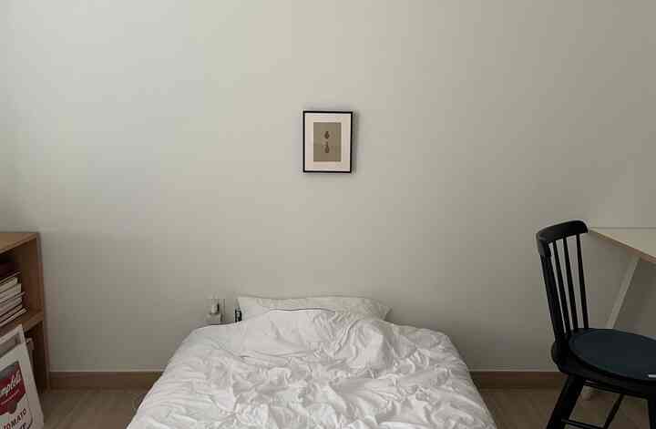 ホワイトトーンの寝室、中央下部にベッドがあり、壁にシンプルな額縁アートが掛かるミニマルな印象的な空間