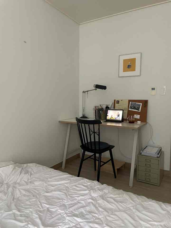 白い壁とナチュラルカラーの床の寝室、シンプルなデスクとテーブルランプ、額縁が配置された集中できる雰囲気のインテリア