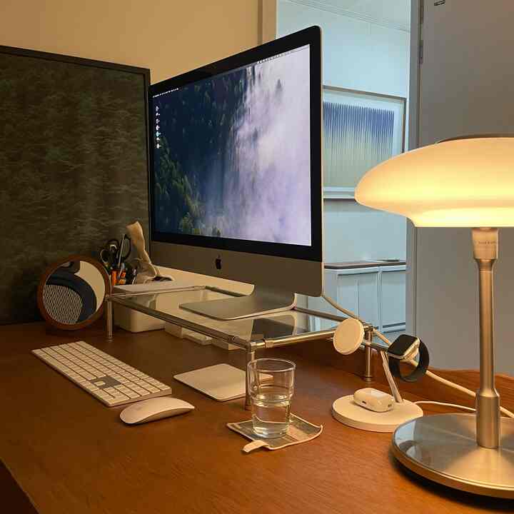 木目調のホームオフィス、整頓された無垢材のデスクにiMacのモニターとシルバーのテーブルランプが配置された落ち着いた雰囲気のインテリア