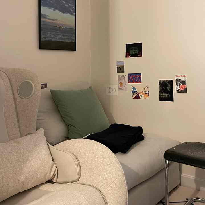 ベージュとグレーのトーンのリビングルーム、リクライニングチェアとソファが配置され、壁にポスターと額縁が飾られた落ち着いた空間