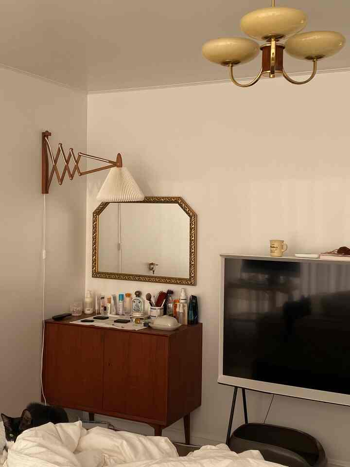 白と木目調が調和したリビング、壁掛け照明やテレビ台、キャビネットと猫がいるシンプルで落ち着いた空間