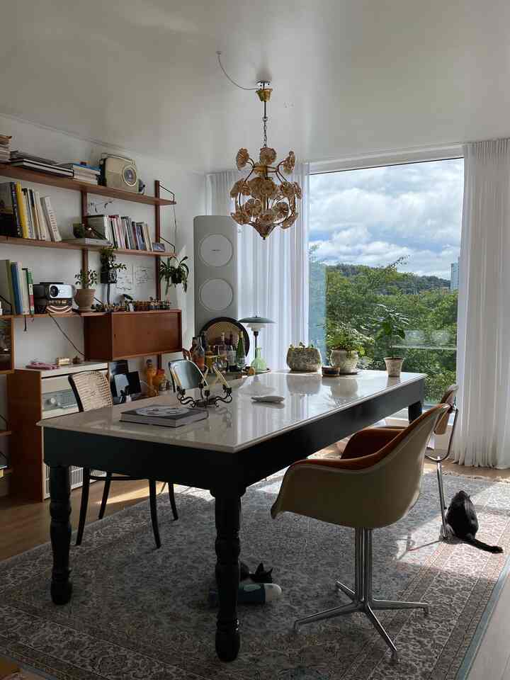 白い壁とカーテンがある明るいリビングに、高級感のある大理石のダイニングテーブルと多様なヴィンテージチェアが配置されたナチュラルな雰囲気の空間