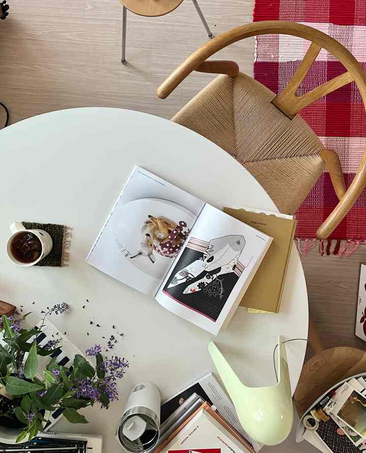 ホワイトと木目調が調和したダイニング空間、丸テーブルと自然な花瓶、赤ピンクのチェック柄ラグが配置されたシンプルなインテリア