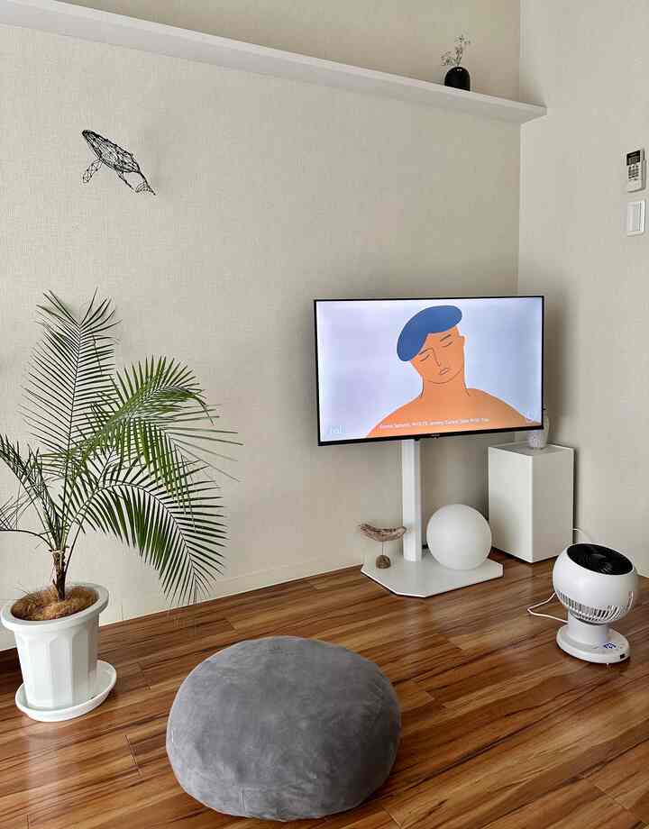 ベージュの壁と木目調の床があるナチュラルカラーのリビング、テレビ台とグレーの丸いクッションが配されたミニマルな空間