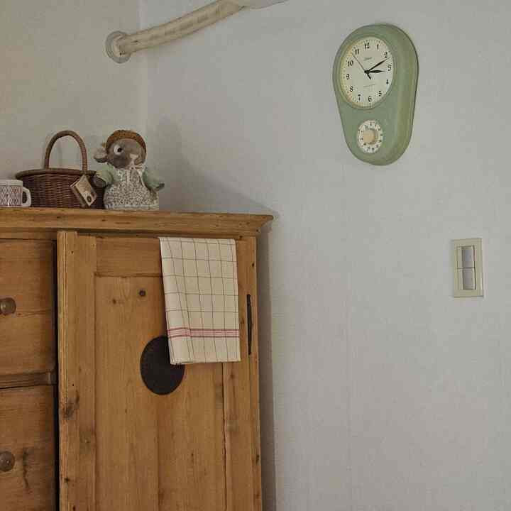 白い壁とブラウンの木製キャビネットがあるヴィンテージスタイルの空間、壁にグリーンのレトロな壁掛け時計が配置されている