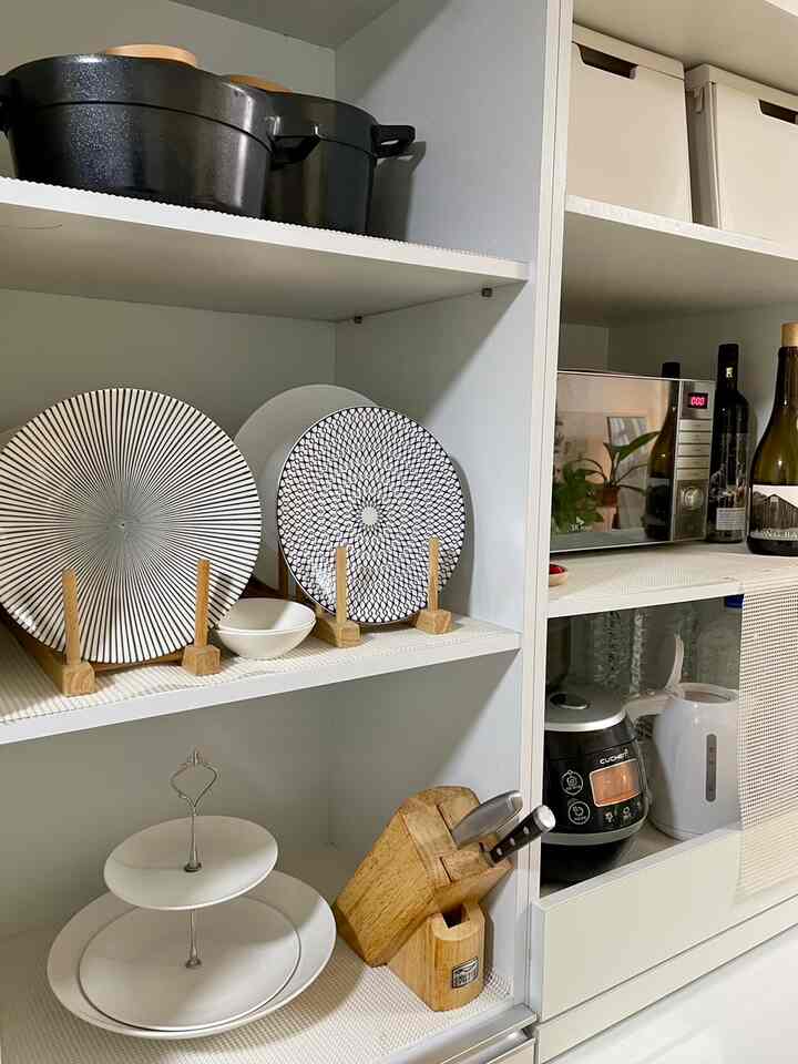 白と木目調のキッチン収納スペース、整然と並んだ皿と電子レンジが配置された雰囲気のあるインテリア
