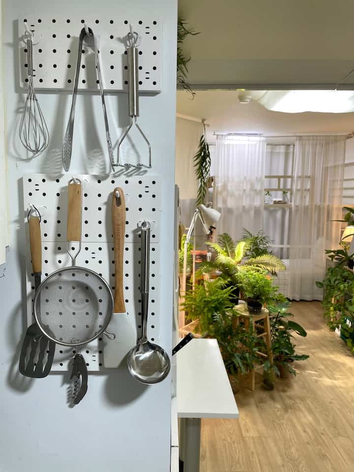 ホワイトの壁と木目調の床が特徴のキッチンスペース、調理器具の収納と豊かな植物が調和するナチュラルなインテリア