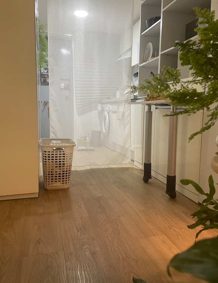 ホワイトと木目調が調和したキッチンと玄関の空間、透けるカーテンが柔らかく空間を仕切るナチュラルモダンなインテリア