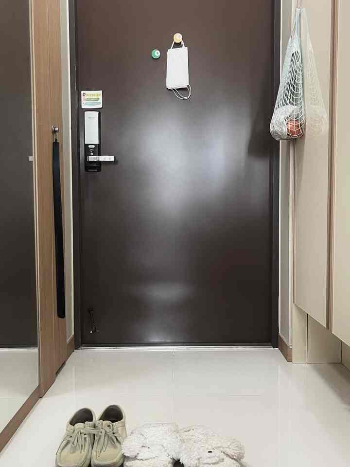 濃いブラウンの玄関ドアと白いタイル床、ウッドトーンのシューズラックが配置された清潔感のある狭い玄関