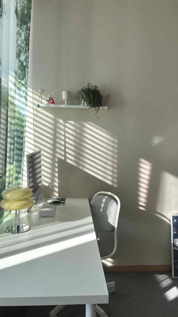 白とベージュのトーンのホームオフィス、すっきりしたデスクとチェア、棚の上に植物が配置された雰囲気のある作業空間