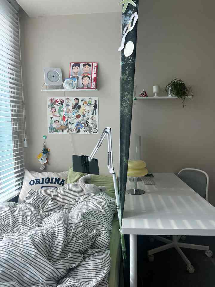 ナチュラルなトーンの一人暮らし用寝室、窓のブラインドと壁棚、デスクとコンピューターが配置された落ち着いた実用的なインテリア