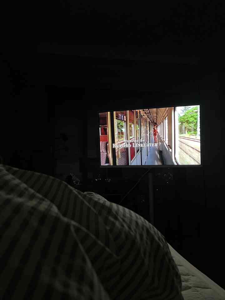 黒とグレーの色調の寝室、居心地の良い寝具とテレビ台が配置された落ち着いた空間