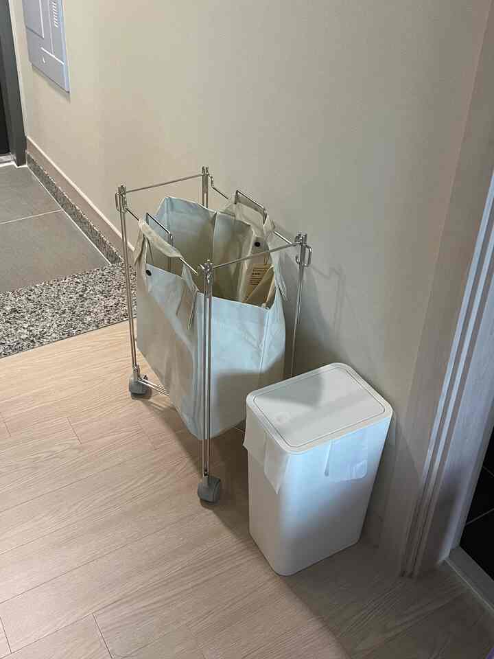 ホワイトとグレーのトーンのキッチンの廊下、ゴミ箱とランドリーバッグが効率的に配置された整然とした空間