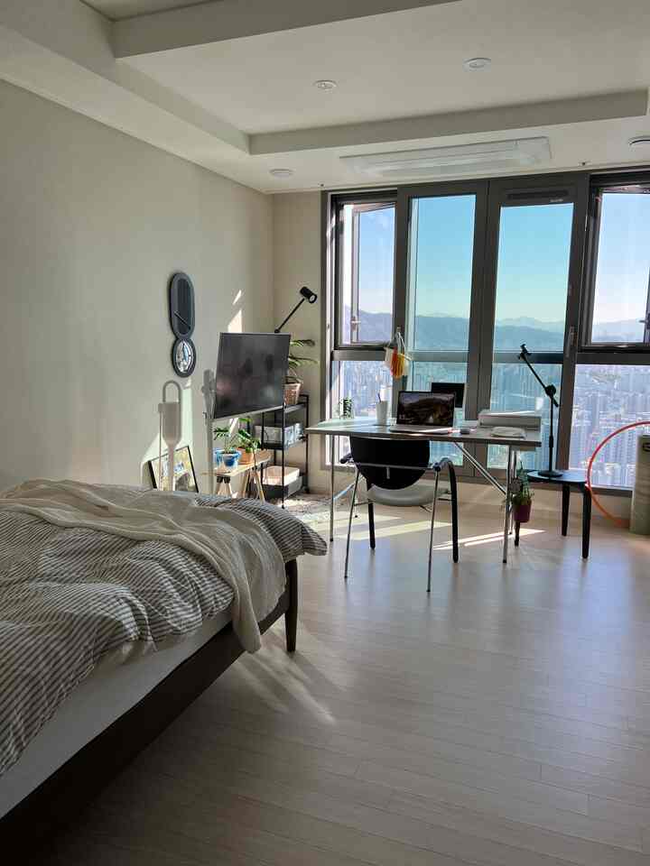 ホワイトと木目調が調和する一人暮らしのアパート寝室、窓際に配置されたデスクとベッドのあるモダンなホームオフィス空間