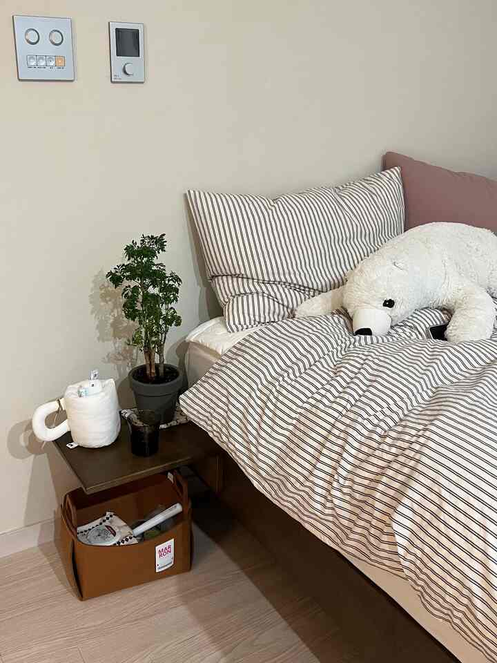 白と茶色のトーンのワンルーム寝室、ストライプの寝具と上質なベッドフレーム、サイドテーブルと収納バスケットが配置された落ち着いた空間