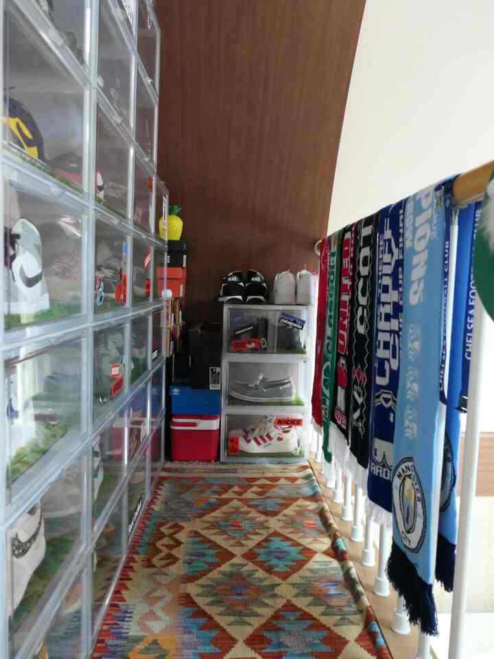 明るい白と茶色の縦長の部屋、透明な靴収納ボックスとカラフルな模様のラグが配置された印象的な空間