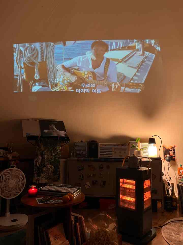暖かい赤色の照明が漂うレトロなリビングルーム、ストーブの上にポットが置かれ、ビンテージ家電とタイプライターが見えます。