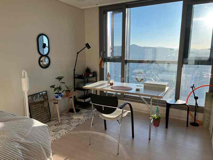 明るいホワイトとベージュのトーンのワンルームのホームオフィス、窓際に大きなデスクが配置され、在宅勤務と自然なインテリアが調和した空間