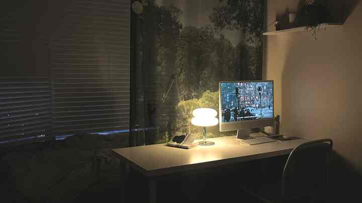 ウッドトーンのブラインドが特徴的なモダンな寝室兼ホームオフィス、デスクライトとコンピュータが配置された落ち着いた空間