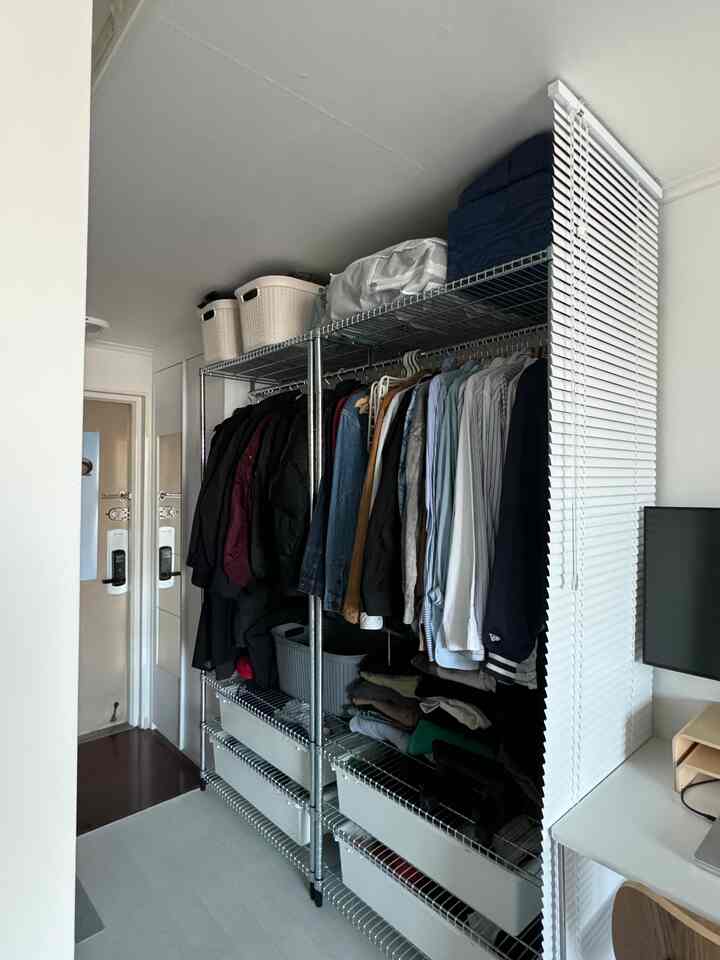 白い壁と天井のあるコンパクトな部屋に、衣類と収納ボックスが整頓されたメタルクローゼットが配置された雰囲気のあるインテリア