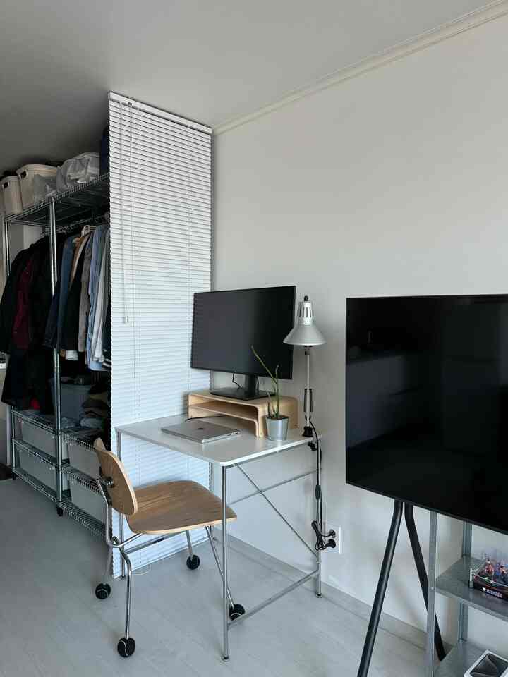 明るい白色調の狭い部屋、コンパクトな白いデスクと木目調チェア、白いブラインドが配置された清潔感のあるホームオフィスのインテリア