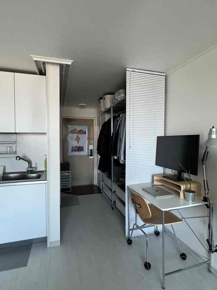 ホワイトと木目調が調和したワンルーム、実用的な収納ラックとコンパクトなホームオフィスが配置された洗練された空間